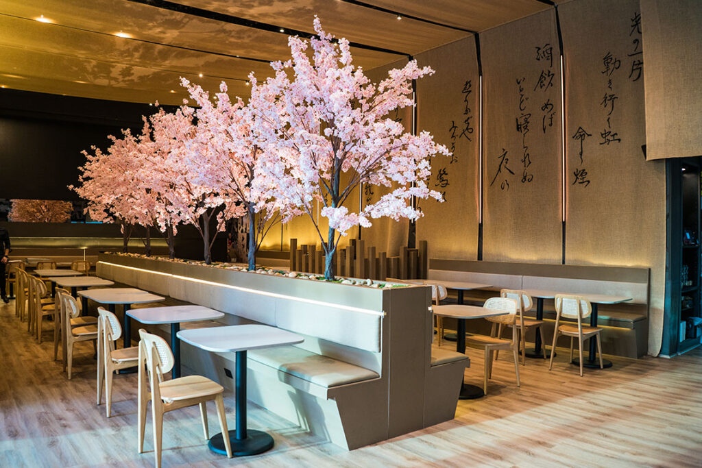  Paperfish Sushi Bar lounge with light wood furniture, cherry trees, and light-colored fabrics on the ceiling and walls with Japanese characters.